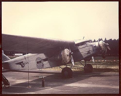 A Pan Am Ford Tri-Motor with engines covered parked on an airport ramp.  Notice the two fire extinguishers under the wing.  Due to stagnant fuel in their components early aircraft engines were prone to start up fires.